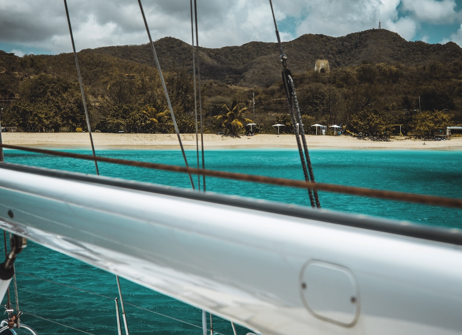 White boom of a sailing yacht in front of azure water and golden sand beach