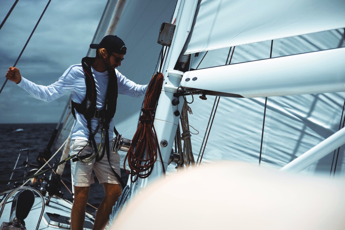 Man wearing a baseball cap and lifejacket at the mast on the deck of a sailing yacht as it heels over