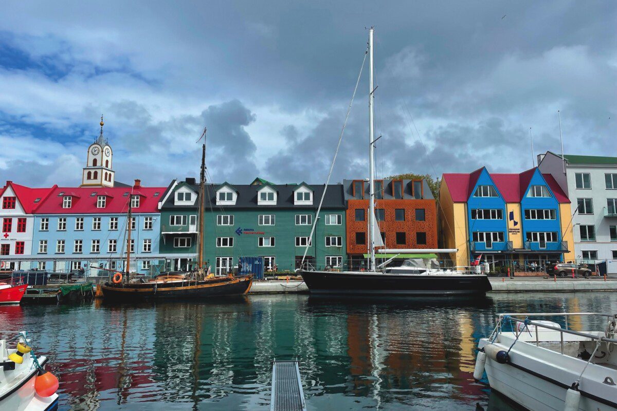 Two sailing yachts tied up to a quayside in front of multi-coloured housing 