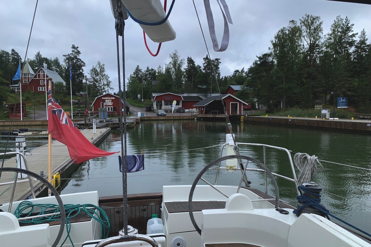 The helm of a sailing yacht looking back towards the shore with red wooden houses