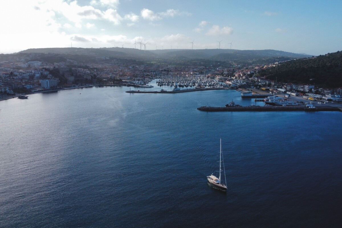 View of a port with a wind farm on the hill and a yacht leaving harbour